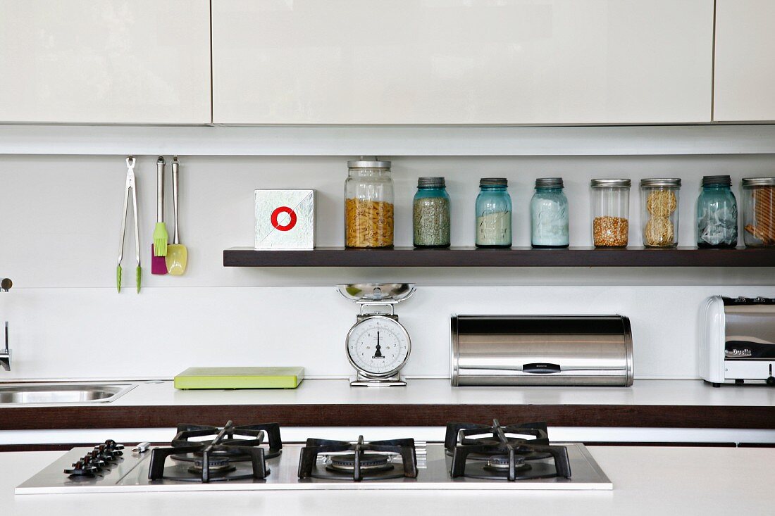 View over the top of a gas stove of a countertop and shelf with screw top jars