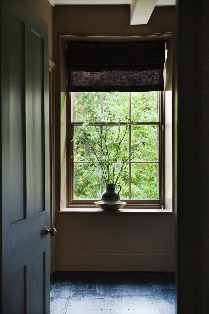 Offenstehende schlichte Kassettentür mit englischem Türknauf; Blick in Vorraum auf Sprossenfenster mit Faltrollo