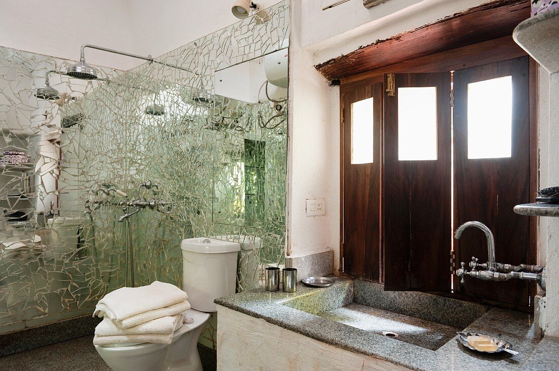 Waschtisch am Fenster mit innenseitigen Holzläden und Duschbereich mit Spiegelmosaik Wandpaneelen