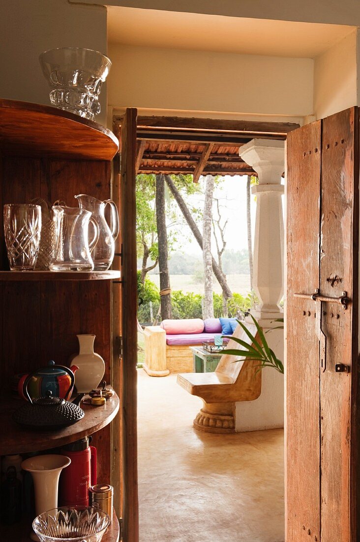Eckregal mit Gläsern neben offener Tür und Blick durch Wohnraum eines indischen Wohnhauses in den Garten