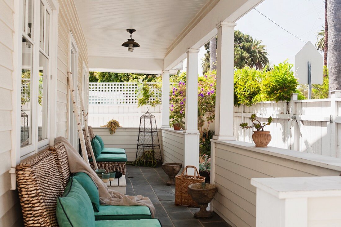 Überdachte Veranda mit weißer Holzverkleidung und Holzsäulen mit Blick über den weißen Gartenzaun