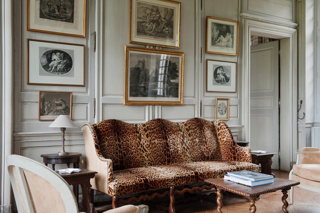 Antique sofa with leopard-skin cover in front of pale, wood-panelled wall and gilt-framed artworks