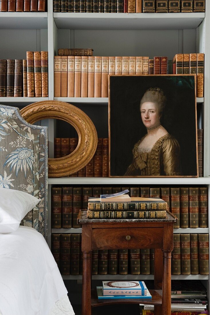 Oil portrait of lady in front of simple shelving holding antiquarian book volumes