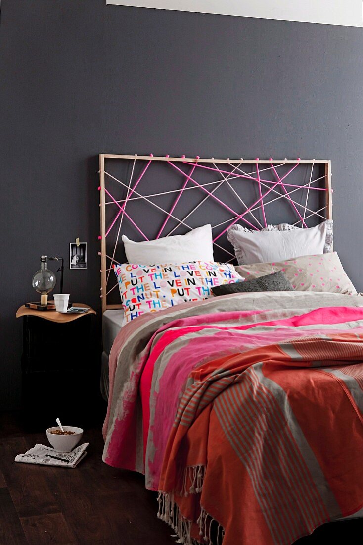 Artistic atmosphere in modern bedroom - bed with headboard made from colourful cords against black-painted wall