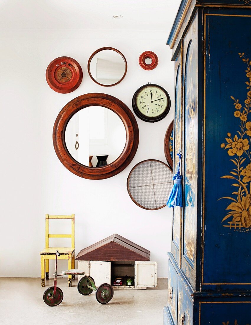 Vintage-style child's bedroom - tricycle and small chair against wall below circular mirrors and wall clock with painted wardrobe to one side