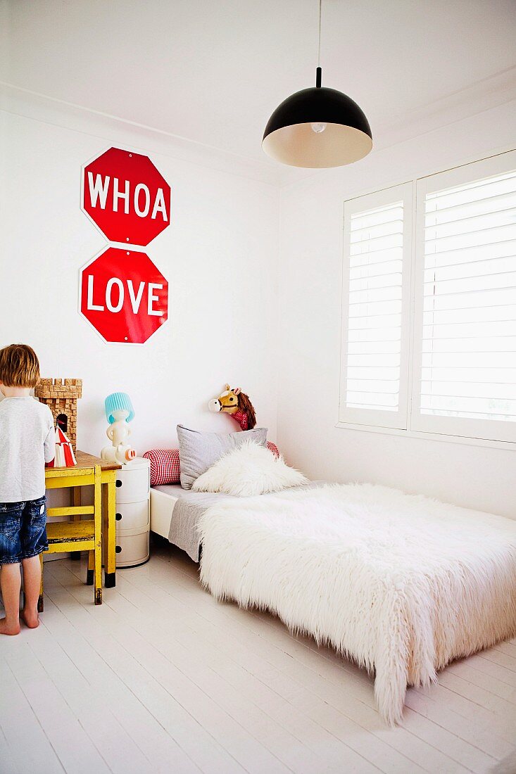 Weisses Kinderzimmer - Bett mit Flokati Tagesdecke am Fenster und kleiner Junge vor Tisch mit Ritterburg