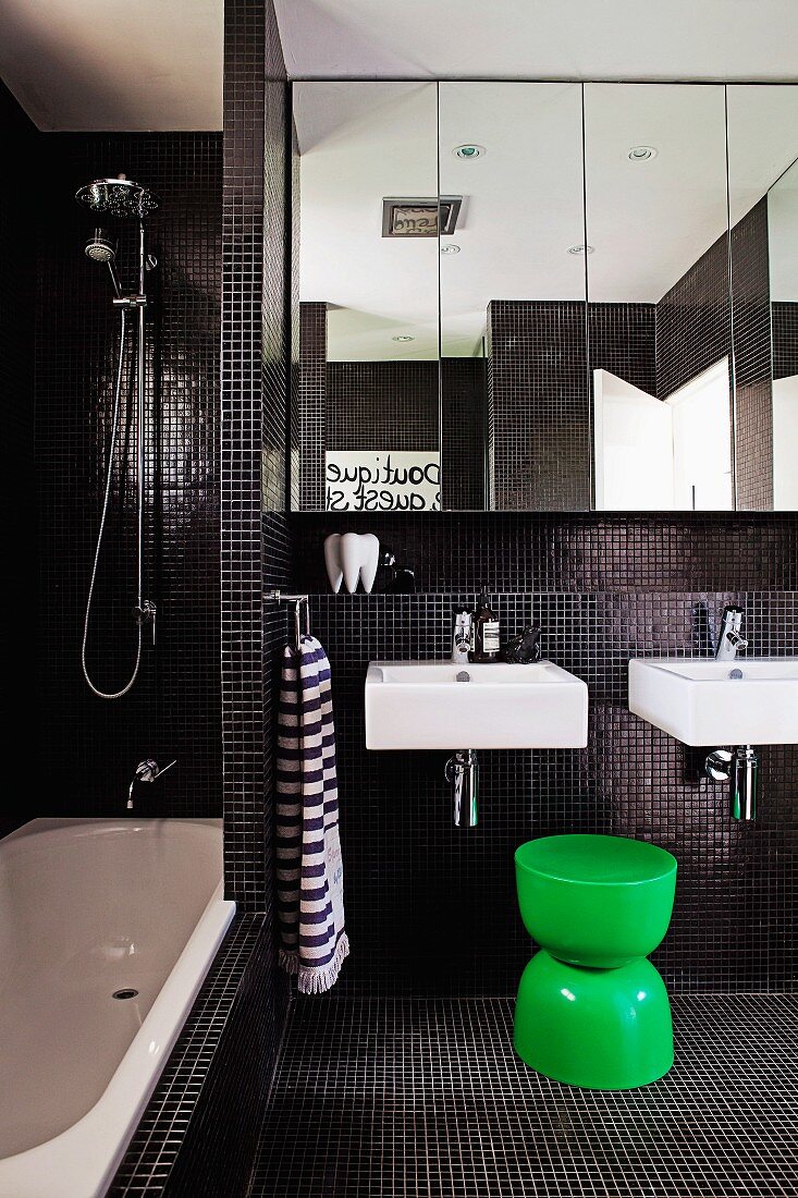 Modernes Bad mit schwarzen Mosaikfliesen und grüner Kunststoff Hocker vor zwei Einzelwaschbecken unter Spiegelschrank