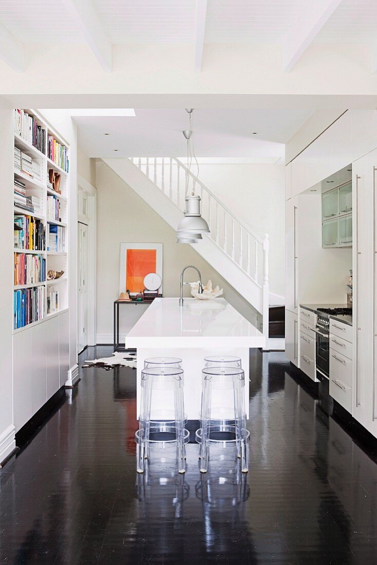 Küche mit weißem Küchenblock und Barhockern aus transparentem Kunststoff auf dunklem glänzendem Holzboden