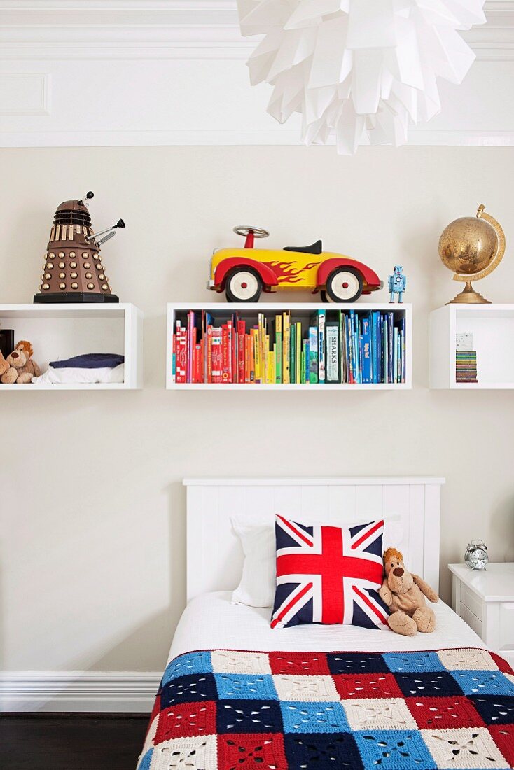 Jugendbett mit englischem Fahnenmotiv auf Kissen unter aufgehängten Regalmodulen an Wand