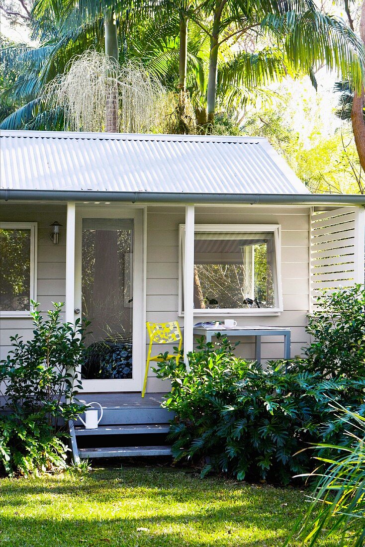 White garden shed with veranda under palm trees