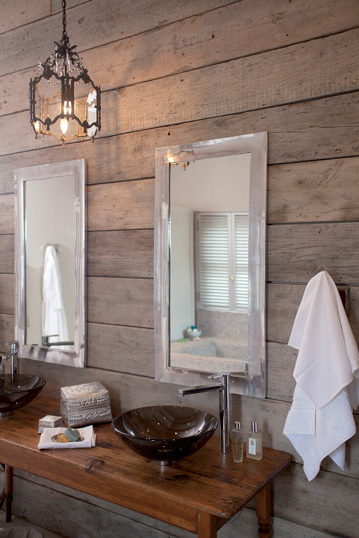 Dunkle Waschschüssel auf Holztisch mit Designer Armatur und Spiegel an rustikaler Bretterwand