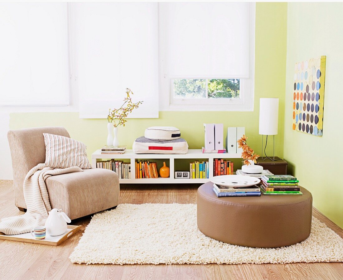 Gepolsterter Bodentisch auf Teppich und Sessel in grün getöntem Wohnzimmer