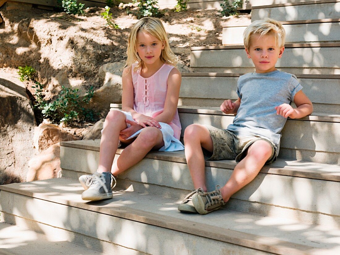 Mädchen und Junge sitzen auf einer Holztreppe im Freien
