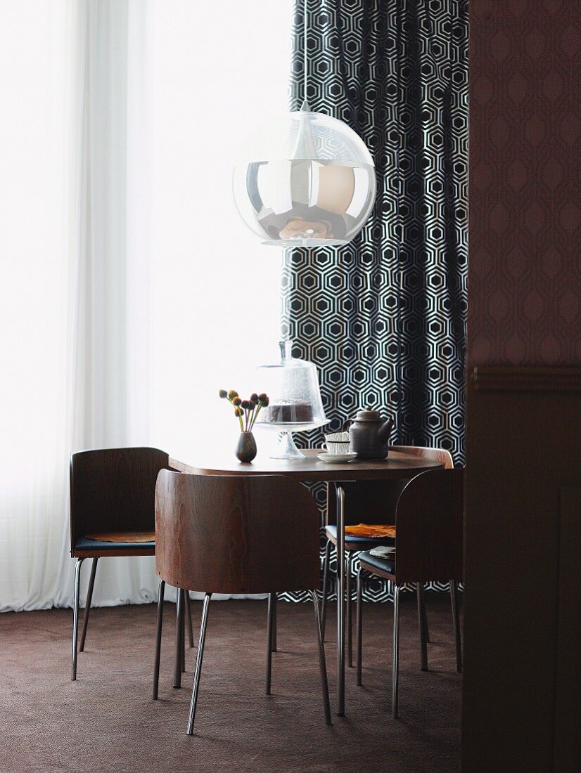 60s-style dining set with brown wooden shell chairs below spherical pendant lamp in front of window with black and white patterned curtain