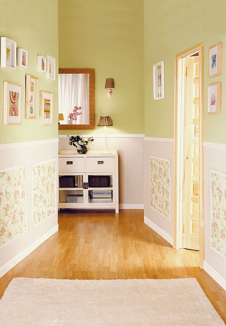 Gallery of pictures on walls painted lime green above panelled dado area in bright hallway