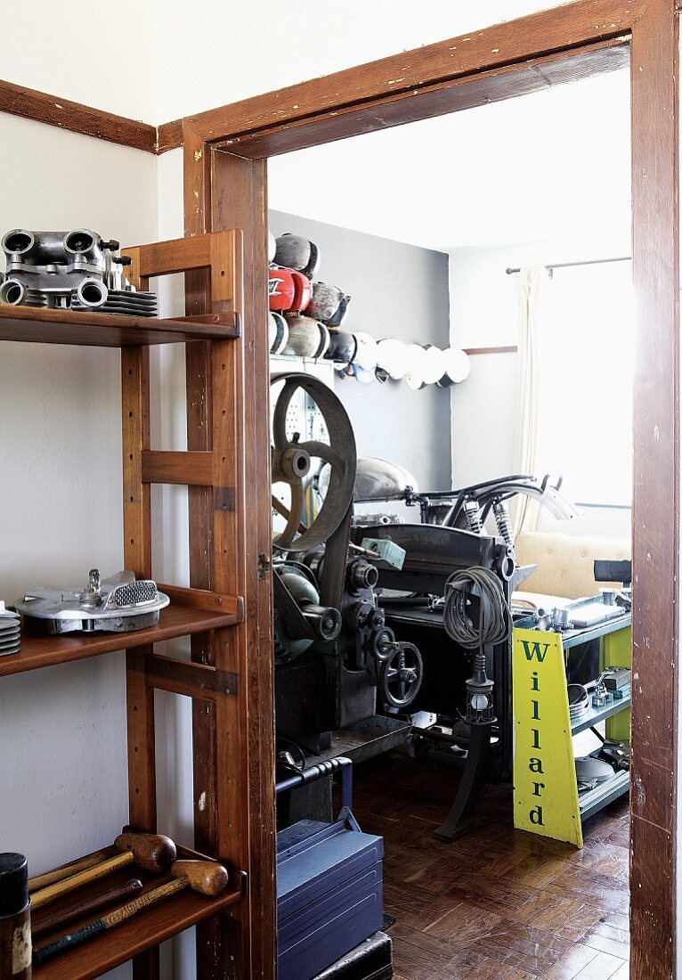 Regal mit Maschinenteilen im Vorraum neben offener Tür und Blick auf Vintage Maschinen