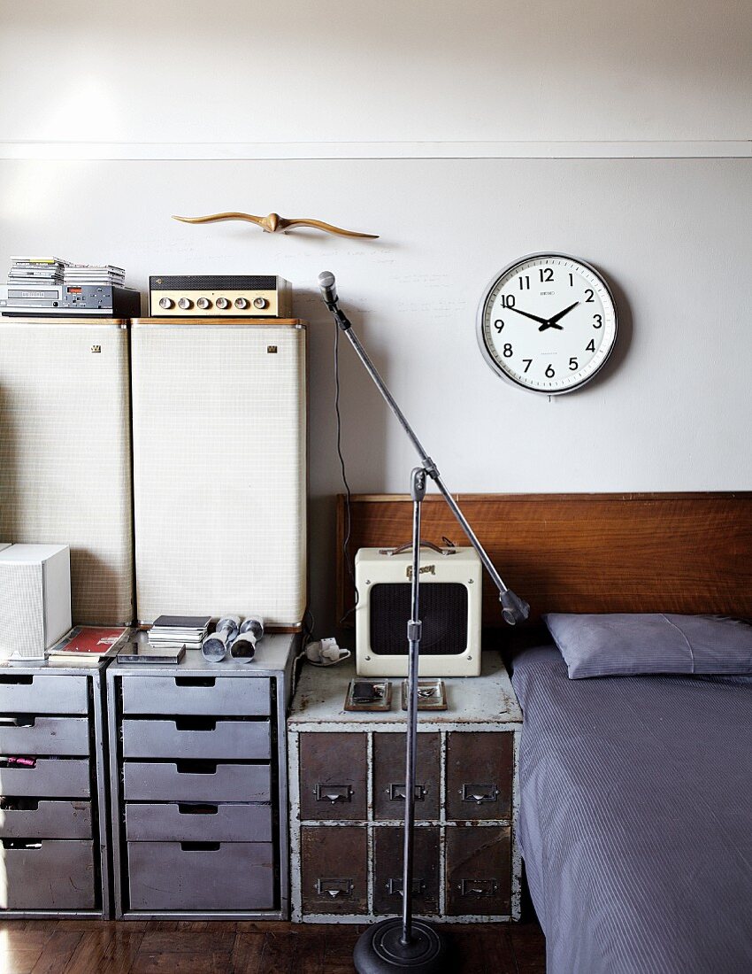 Stereo equipment on drawer cabinets in various styles next to bed with headboard below clock on wall