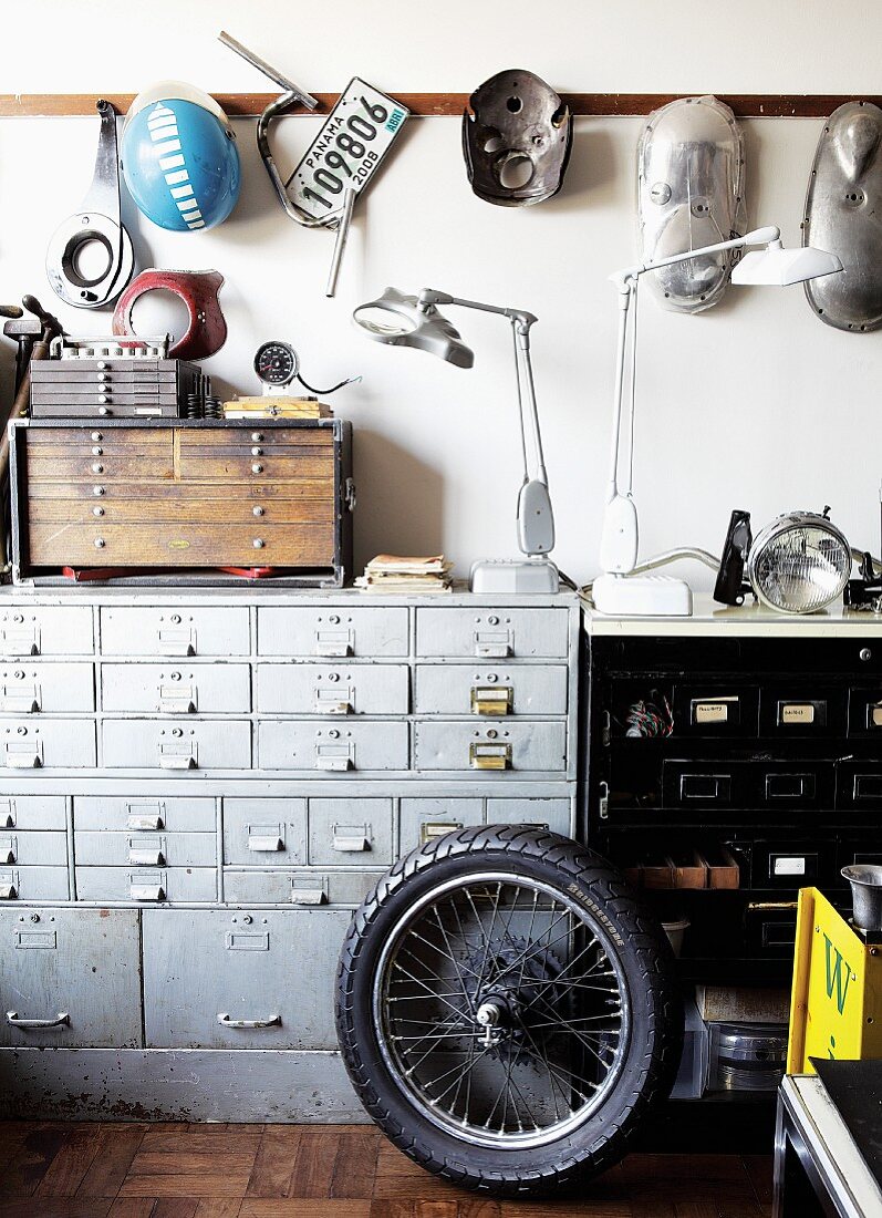 Motorbike wheel in front of vintage chest of drawers and sheet metal components hanging on wall