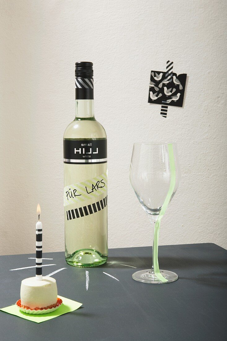 Small cake, candle and bottle of wine decorated with washi tape