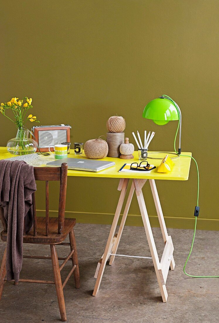 Vintage chair, bright yellow desk on trestles and lime green lamp against olive green wall