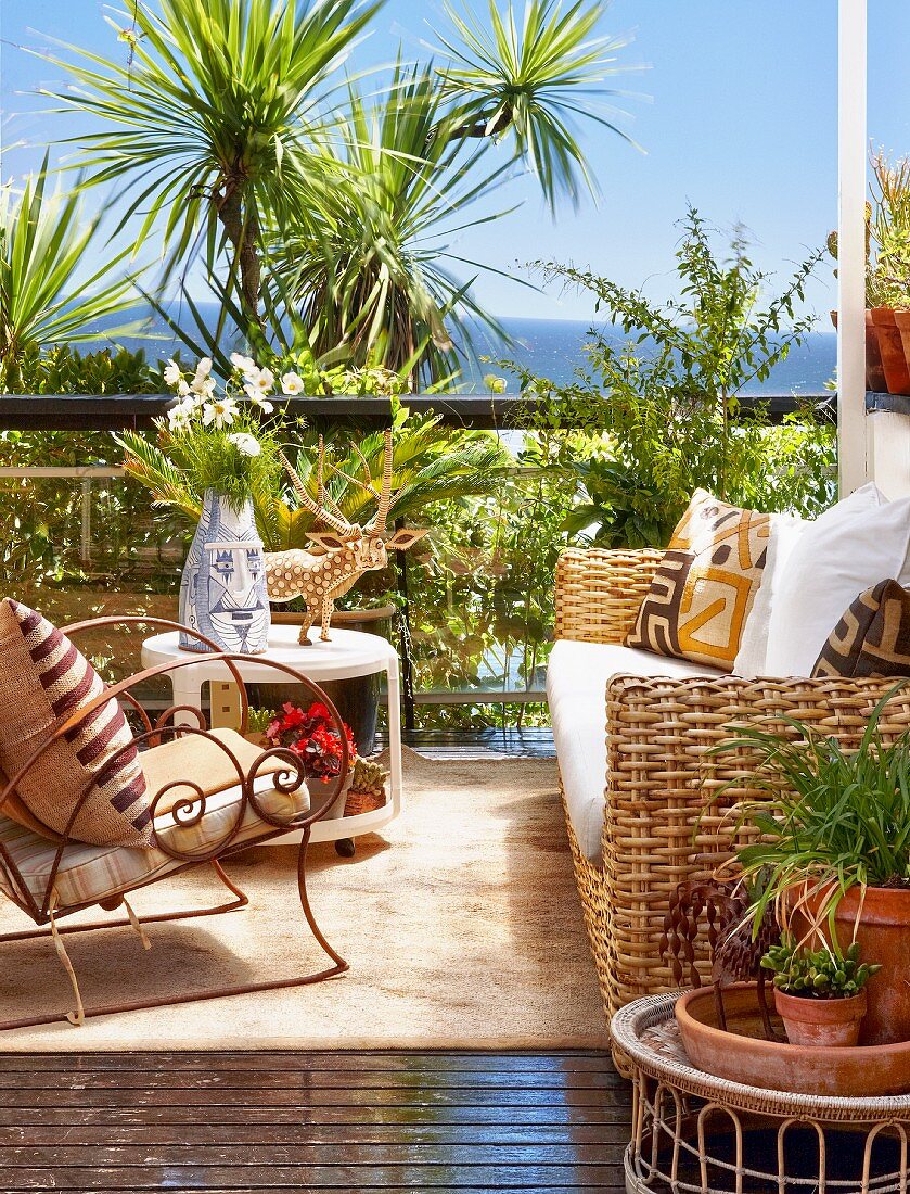 Sonniger Terrassenplatz - Rattan Sofa und Sessel aus geschwungenem Metallgestell vor Palmengarten am Meer