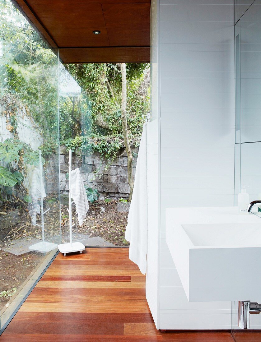 Modernes Waschbecken in offenem Waschbereich vor Glasfassade eines Wohnhauses mit Gartenblick
