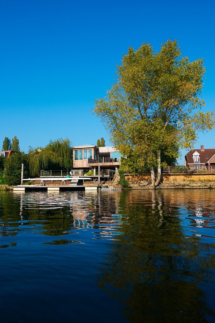 Contemporary house on river bank with landing stage and mature trees