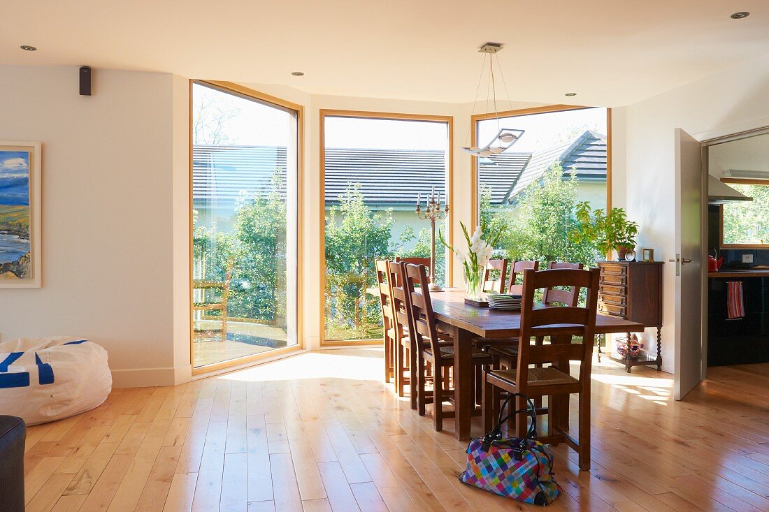 Sonniger, großzügiger Essraum mit drei raumhohen Glasfronten, Parkettboden und einer Esstafel mit Stühlen aus Massivholz
