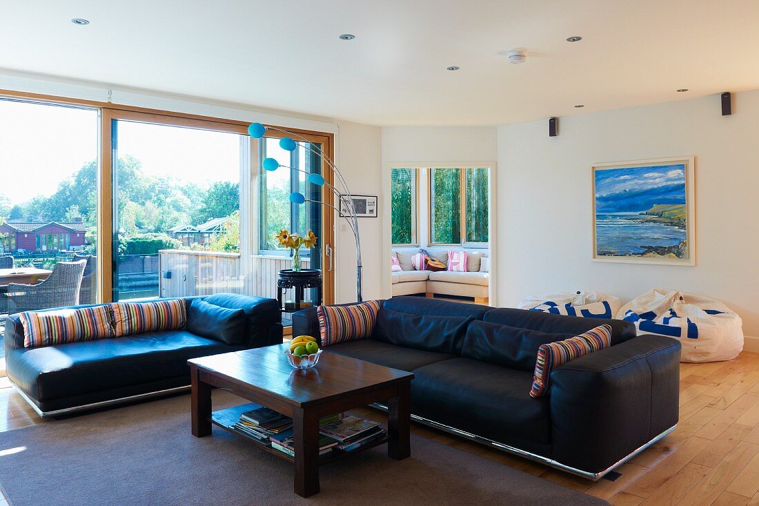 Sitzlandschaft mit schwarzen Ledersofas, grauem Wollteppich und einfachem Holz-Couchtisch in geräumigem Wohnzimmer mit großer Glasfront