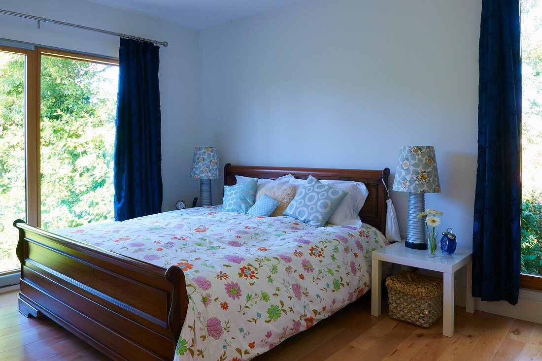Traditionelles Doppelbett mit geblümter Bettwäsche in zeitgenössischem Schlafzimmer mit großen Fensterfronten