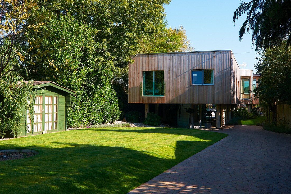Blick auf modernes, auf Holzstützen stehendes Holzhaus mit gepflegter Gartenanlage
