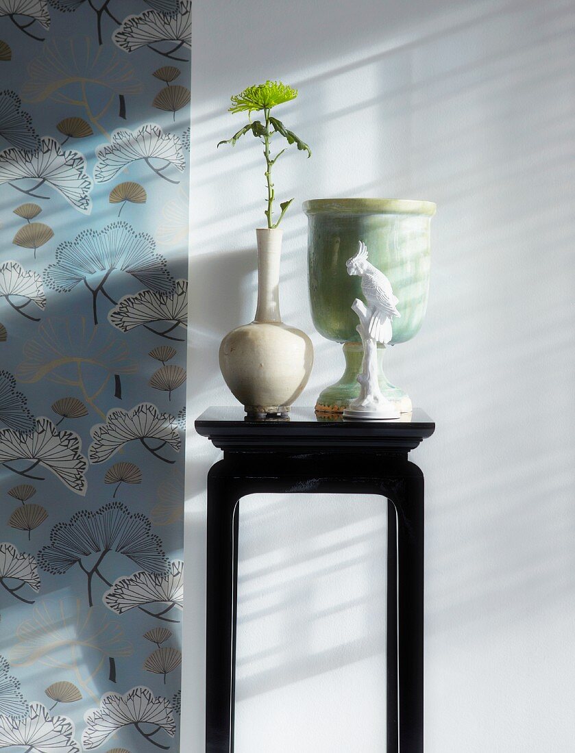 Vases on small console table next to Chinese-style floral wallpaper
