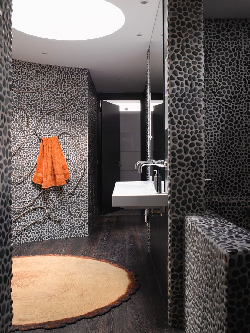 Designerbad mit dunklem Kieselmosaik raumhoch gefliesten Wänden und geschwungener Wand