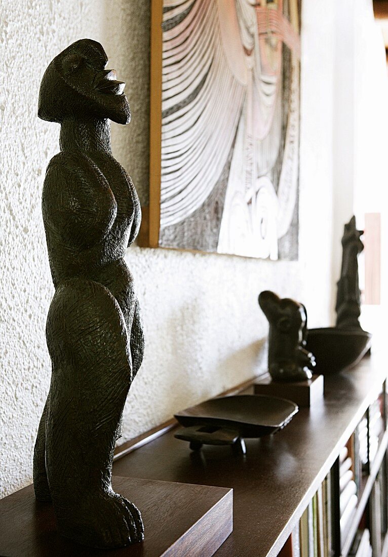 Afrikanische Skulpturen aus Holz neben Bild an Wand auf sideboardartigen Regalschrank