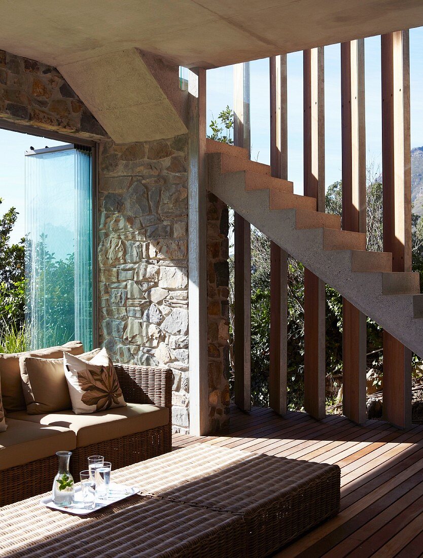 Tisch und Sofa aus Rattan in Wohnraum mit rahmenlosen Schiebefenstern und verstellbaren Holzlamellen als Sonnenschutz