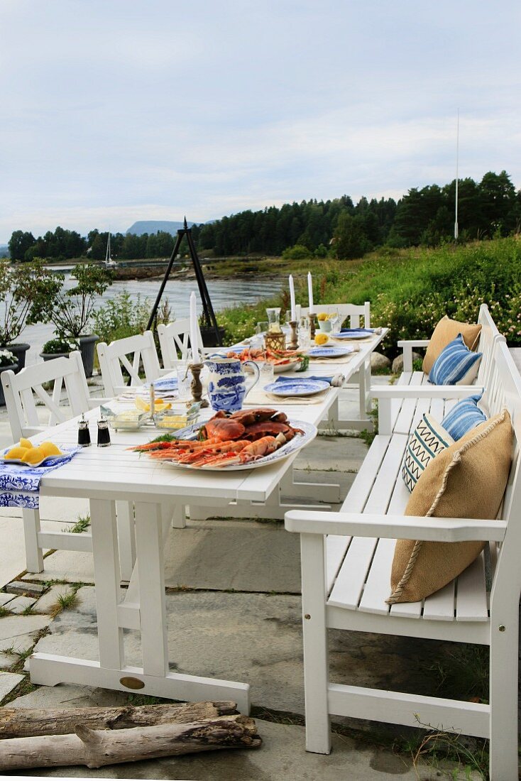 Festively set garden table with robust, white, country-house-style wooden furniture on lakeside terrace