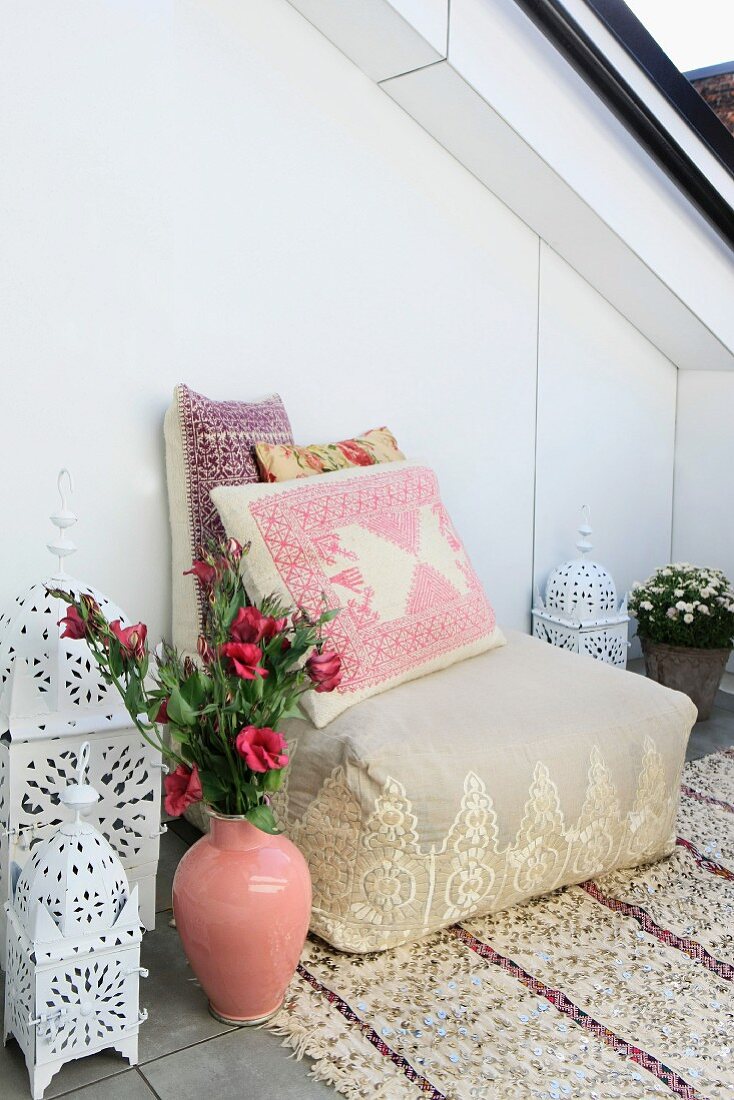 Sitzpolster mit bestickten Kissen auf Paillettenteppich, marokkanische Keramikvase und Laternenleuchten als orientalische Ausstattung einer modernen Dachterrasse