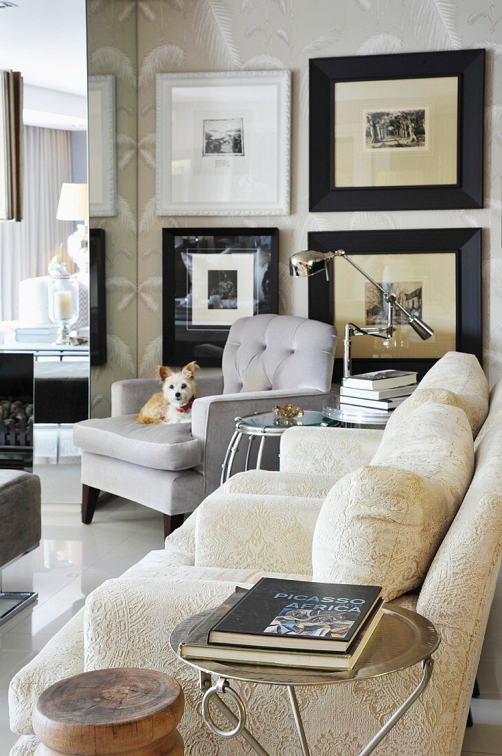 Wohnzimmer mit hellen Polstermöbeln, Beistelltischen und großen schwarz gerahmten Bildern an der Wand