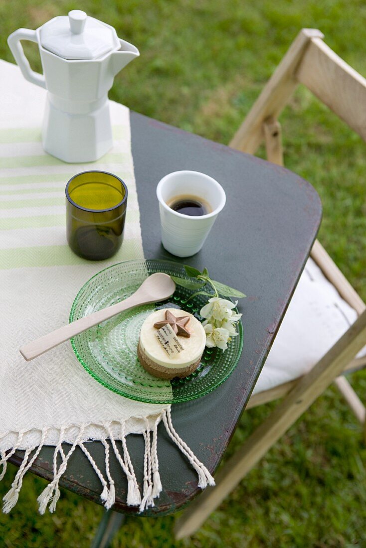 Espressokanne, Becher mit Kaffee und Glasteller mit süssem Gebäck auf einem Gartentisch