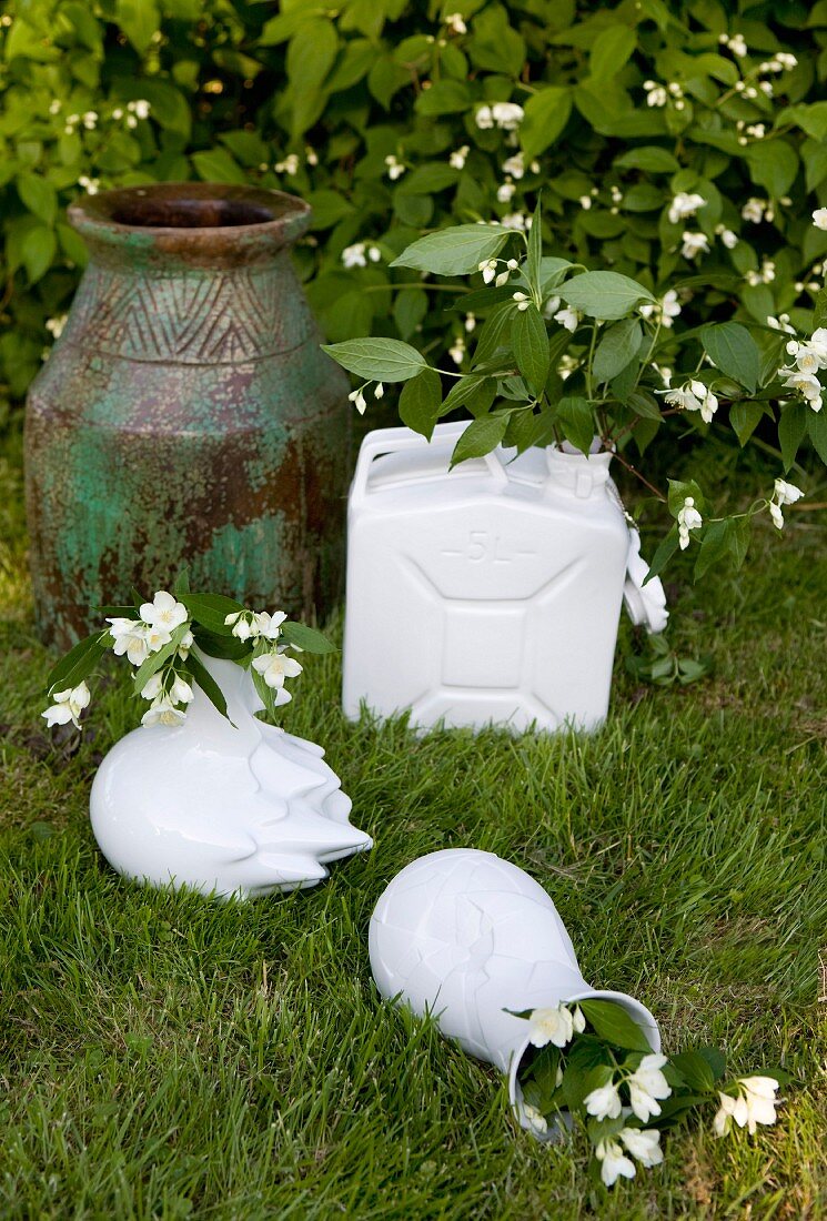 weiße Vasen und ehemaliger Kanister mit Jasmin Blumenzweigen neben Bodenvase im Garten