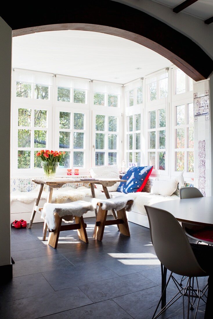 Gemütliche Eckbank mit Schaffellen, Holztisch und Hockern im Wintergarten mit Sprossenfenstern