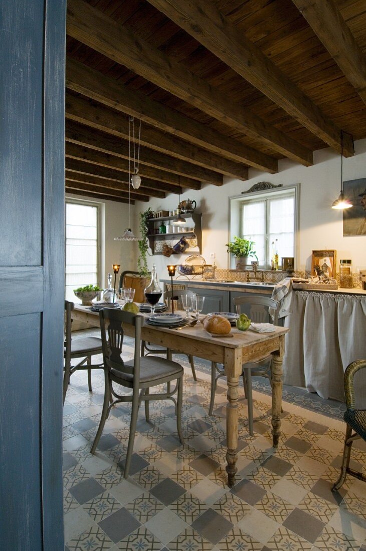 Chequered, tiled floor in cosy, country-house kitchen with vintage furnishings and low, wood-beamed ceiling