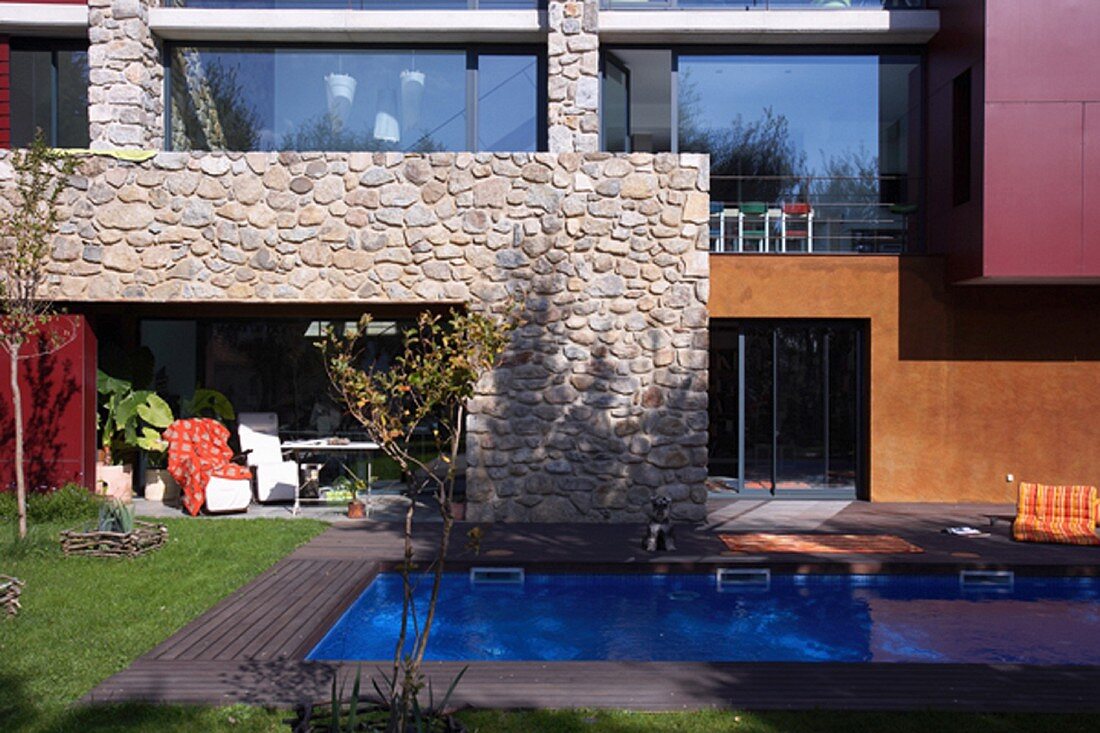 Swimmingpool im Garten vor modernem Gebäude mit Natursteinwand