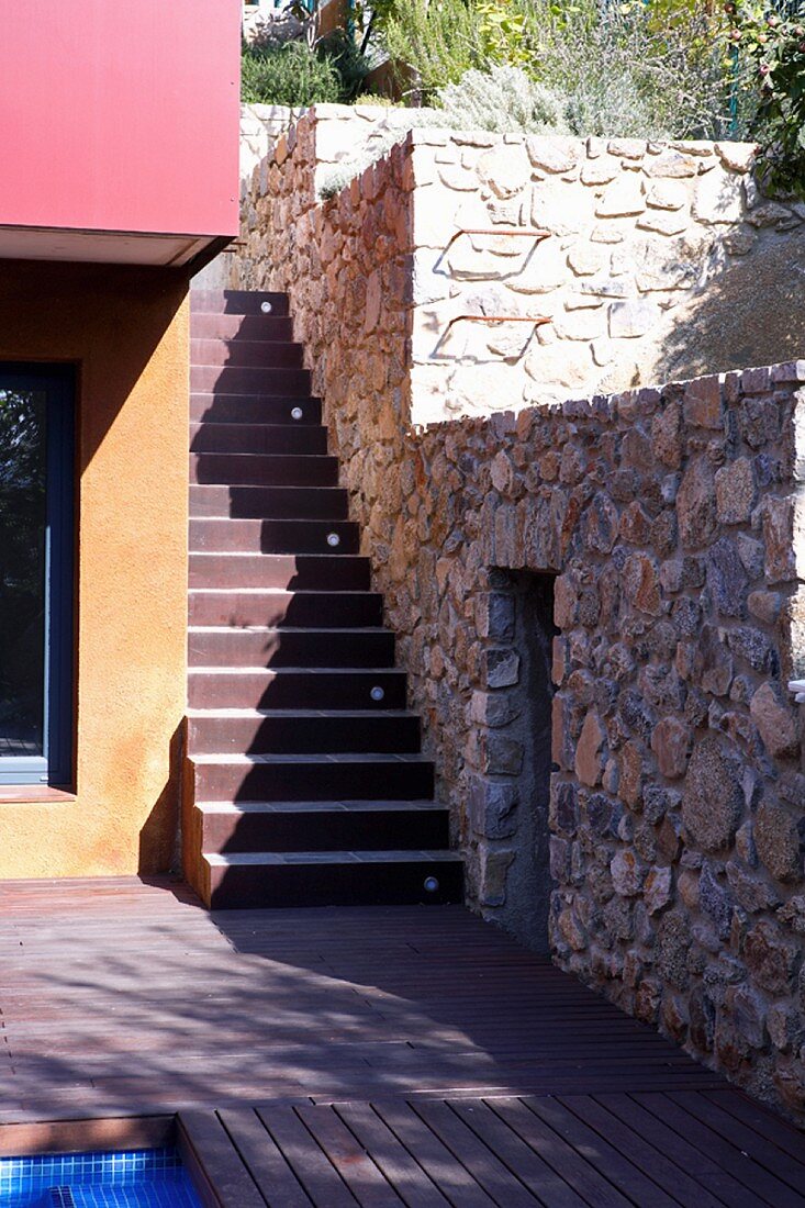 Treppenaufgang zwischen Haus und breiter Natursteinmauer mit kleinem Durchgang