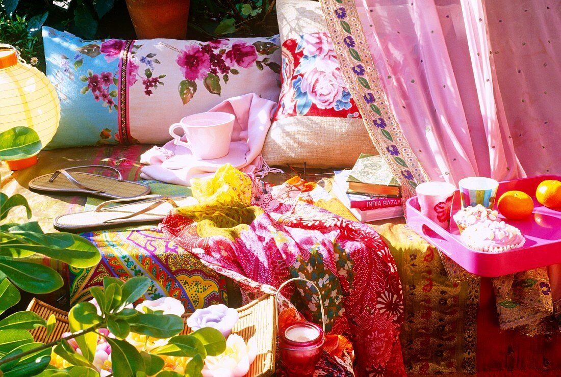 Colourful throws on bench, flip-flops, teacup and cushions in garden