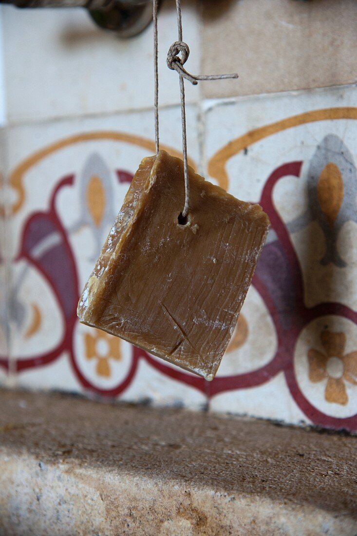 Naturseife an einer Schnur, aufgehängt vor den originalen Musterfliesen einer südfranzösischen Küche