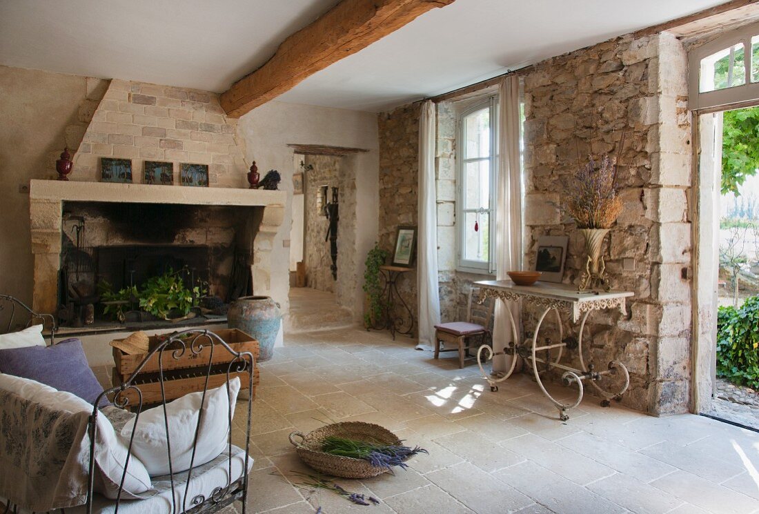 Wohnraum in restauriertem Landhaus mit russgeschwärztem Kamin und zierlichen, französischen Metallmöbeln vor rustikalen Natursteinwänden