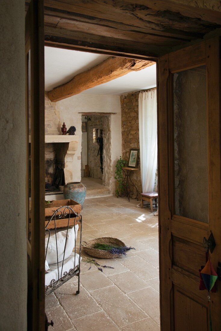 Blick durch offene Tür in den Wohnraum eines südfranzösischen, restaurierten Landhauses mit rustikalem Natursteinboden