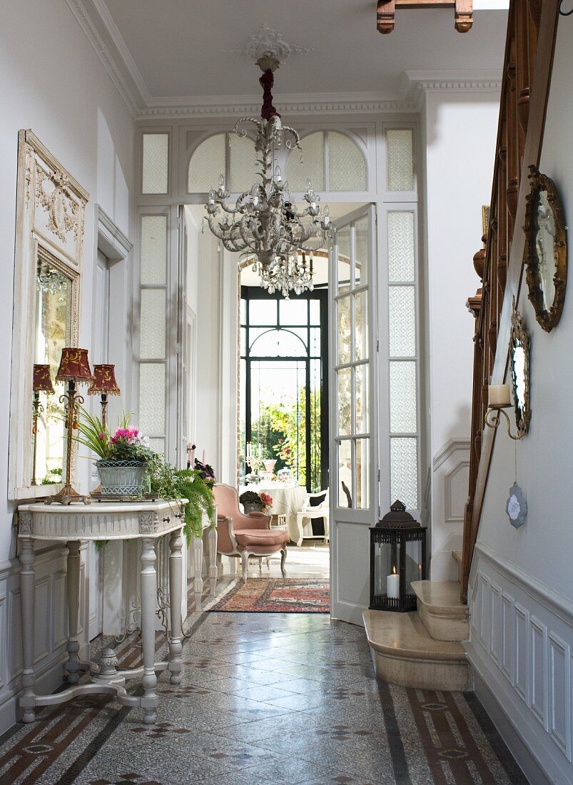 Elegante Diele mit barockem Wandtisch, Kronleuchter und Treppenaufgang mit Steinstufen und Holzgeländer