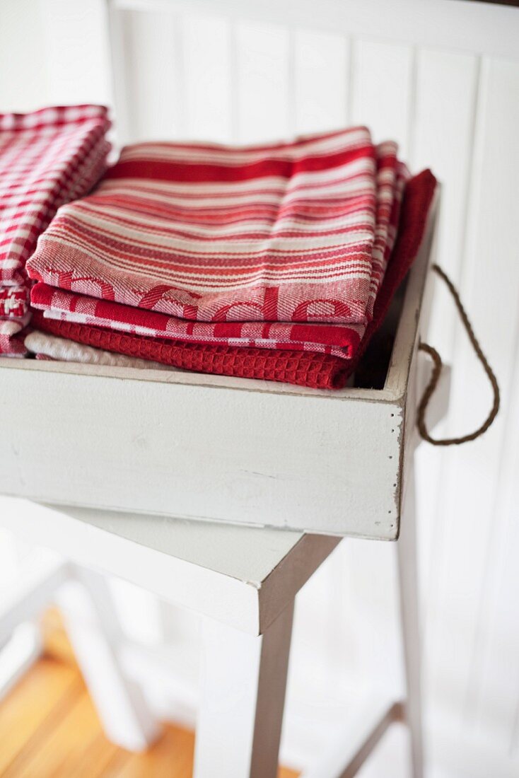 Stacked dish towels in a white vintage box on a stool